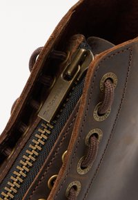 Bottes en cuir marron avec fermeture éclair sur le côté, œillets en métal et lacets marron foncé. Cuir texturé avec une finition vieilli et panneau en toile.