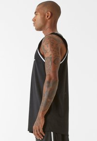 Melnas sporta tvertnes krekls ar baltu apdari, izgatavots no elpojoša auduma. Tam ir brīva piegriezuma forma un izliekts apakšmalas, izceļot tetovējumus uz rokas.