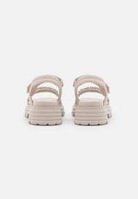 Sandales rose clair avec des sangles ajustables, un talon rembourré et une semelle en caoutchouc texturée présentant des crêtes superposées et un détail accent transparent.