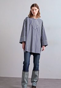 Tunic lunga a strisce blu navy e bianche con maniche ampie e scollatura a strati, abbinata a jeans in denim scuro e gambaletti grigi in contrasto.
