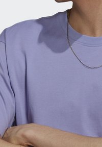 Levandulové tričko s kulatým výstřihem a jemnou texturou, krátkými rukávy a vroubkovaným detailem na límci, kombinované se stříbrným řetízkem.
