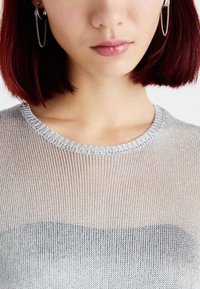 Prozirni srebrni pleteni top s rebrastim izrezom, koji prikazuje prijelazni efekt od svijetle do tamne nijanse. Minimalistički dizajn, meke teksture.