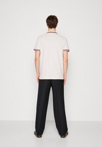 Polo gris clair avec détails de col rayé en rouge et marine. Associé à un pantalon noir ample. Tissu en coton lisse.