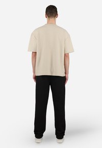 Chemise beige texturée à manches courtes associée à un pantalon noir à côtes et des chaussures de couleur claire, vue de dos.
