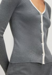 Grijze geribde cardigan met lange mouwen, voorzien van een V-halslijn en witte knopenlijst, gemaakt van een zachte, textuurstof.