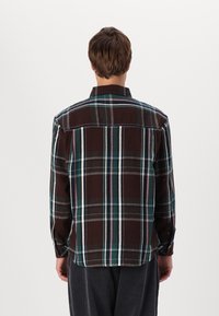 Brown and green plaid flannel shirt with a pointed collar, button cuffs, and dual back yoke detailing. Cotton blend fabric, textured finish.
