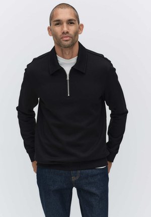 Svart sweatshirt med dragkedja i kragen, med en slät textur och långärmar, tillsammans med blå jeans.
