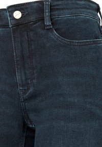 Gros plan de jeans en denim bleu foncé à l'avant avec bouton métallique, passants de ceinture, poche avant et détails de couture visibles.
