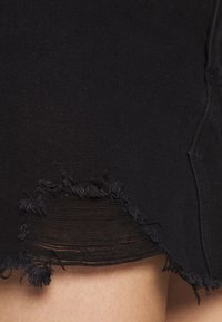 Svart denimkjol med fransad nederkant och slitna detaljer, med en mjuk textur och en kroppsnära design.