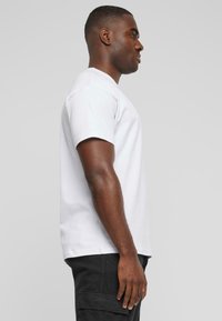 White cotton t-shirt with short sleeves, a crew neck, and a relaxed fit, worn with dark cargo shorts, shown from the side.