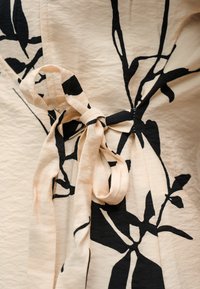 Tissu beige avec imprimé floral abstrait noir, avec une ceinture en tissu nouée autour de la taille.