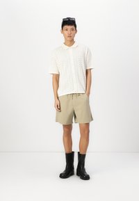White short-sleeve polo shirt with textured zigzag pattern, paired with beige shorts and black knee-high boots. Accessories include sunglasses.