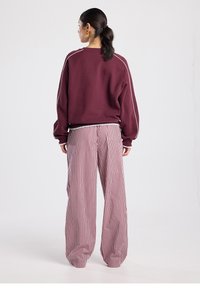 Maroon sweatshirt with relaxed fit and white piping, paired with wide-legged red and white striped pants, shown from the back.