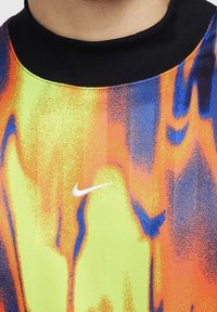 Krótkosleeve koszula w wielu kolorach z czarnym kołnierzykiem. Projekt zawiera żywe wzory w kolorze żółtym, pomarańczowym i niebieskim. Zawiera logo Nike.