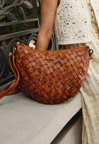 Braune, gewebte Lederhandtasche mit einer lässigen Form, ausgestattet mit einem Reißverschluss und einem verstellbaren Tragegurt. Fein strukturierte Oberfläche und weicher Abschluss.