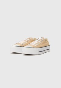 Beige lærduk sneakers med lav profil, hvit gummisåle og svart stripe. Har hvite snørebånd og metalliske snører. Teksturert tåhette.