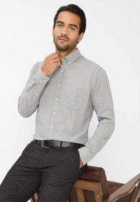 Grijze en witte geblokte blouse met lange mouwen, een button-down kraag en een enkele borstzak, gecombineerd met donkere, gestructureerde broeken en een zwarte riem.