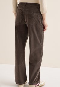 Pantaloni in velluto a coste marroni con design dritto, presentano due tasche posteriori e una superficie tessurizzata, abbinati a calzature casual.