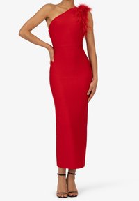 Robe rouge à une épaule avec une silhouette ajustée, ornée d'accents en plumes sur une épaule. Fabriquée en tissu extensible, atteignant le mi-mollet.