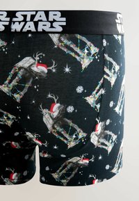 Czarne bokserki Star Wars z motywem świątecznym, na których znajdują się AT-AT w czapkach Mikołaja, udekorowane lampkami choinkowymi i płatkami śniegu.
