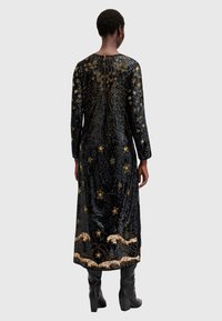 Rochie lungă din catifea neagră, cu broderie aurie în formă de stele și paiete, având o pliere la spate și modele detaliate cu lei și valuri.