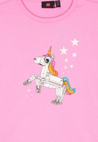 Un tricou roz cu un grafic ce prezintă un unicorn robotic cu o coamă multicoloră și un corn auriu în formă de con, pe un fundal de motive cu stele.