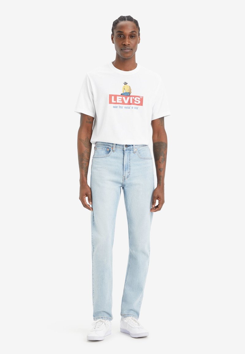 Witte T-shirt met korte mouwen en een rood Levi's-logo, gecombineerd met lichtblauwe rechte jeans en witte sneakers.