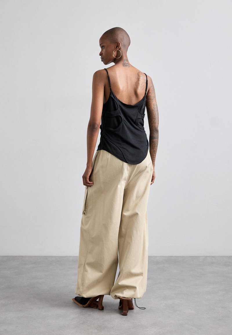 Schwarzes, rückenfreies Tanktop mit dünnen Trägern, kombiniert mit beigen, weit geschnittenen Hosen. Die Schuhe haben ein Blockabsatzdesign. Glatte Textur und lockere Passform.