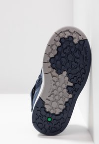 Podešev boty má tmavě navy modrou gumovou konstrukci s hexagonálními vzory. Obsahuje texturovanou šedou mezipodrážku označenou "Neznačkování."