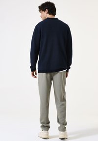 Marineblauer Strickpullover mit lockerer Passform und langen Ärmeln, kombiniert mit hellgrauen schmal geschnittenen Hosen und weißen Sneakern. Einfaches strukturierte Design.