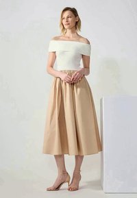 Avskåret topp med ribber i hvit, kombinert med en beige, knelangs plissert skjørt. Gjennomsiktige hælsandaler fullfører antrekket.