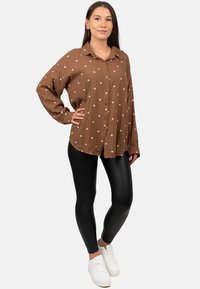 Brown button-up shirt with small white heart patterns, long sleeves, and relaxed fit, paired with black leggings and white sneakers.