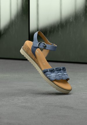 Sandale bleue avec détail volanté en couches, semelle intermédiaire en liège et bride de cheville réglable. Semelle texturée pour l'adhérence, doublure intérieure lisse.