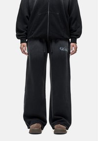 Zwarte katoenen oversized hoodie met rits en voorzakken, gecombineerd met zwarte sweatpants met een grafisch logo, een relaxte pasvorm en een trekkoord in de taille.