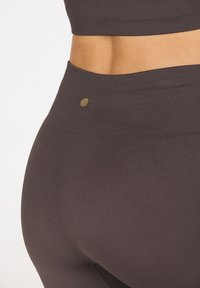 Dunkelgraue gerippte Leggings mit hohem Bund, die ein kleines goldfarbenes Logodetail aufweisen. Die glatte Textur und das enganliegende Design verbessern den Komfort.