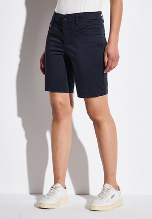 Navyblauwe shorts met een rechte snit en twee zijzakken. Voorzien van een knoopsluiting en gestikte zoom voor duurzaamheid. Gedragen met witte sneakers.