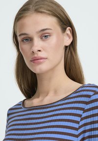 Blå og brun stribet top med rund halsudskæring og blødt, tekstureret stof. Striberne er horisontalt justeret med en let glans.