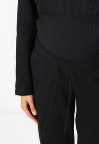 Ropa de maternidad de lounge negra, con una tela suave y elástica, cinturilla elástica con cordón y mangas largas para mayor comodidad y flexibilidad.