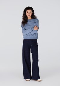 Lichtblauwe sweatshirt met ronde hals en oversized pasvorm, gecombineerd met zwarte wijde broek met subtiele patroondetails. Witte schoenen.