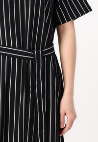 Vestido com riscas pretas e riscas brancas verticais, mangas curtas, cintura ajustada com um cinto combinando e tecido texturizado.