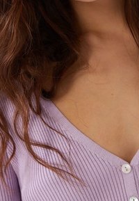 Fialkově fialový žebrovaný kardigan s výstřihem do V a třemi knoflíky, který představuje jemnou texturu a lehkou látku.