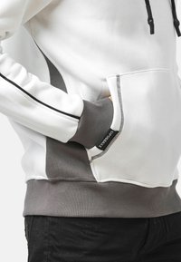 Weißes Sweatshirt mit grauen Akzenten, einer Kängurutasche und kontrastierenden Nähten. Das Material ist weich, mit gerippten Bündchen und Saum.