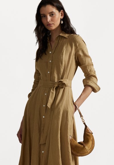 Robe chemise en lin khaki avec une ceinture, devant boutonné, manches longues et finition texturée. Associée à un petit sac à main en suede marron.