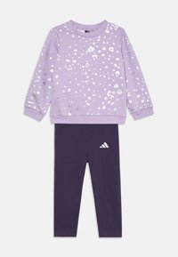 Fialová mikina s dlhým rukávom so striebornými leopardími škvrnami a logom, v kombinácii s tmavo fialovými legínami s malým bielym logom na nohe.