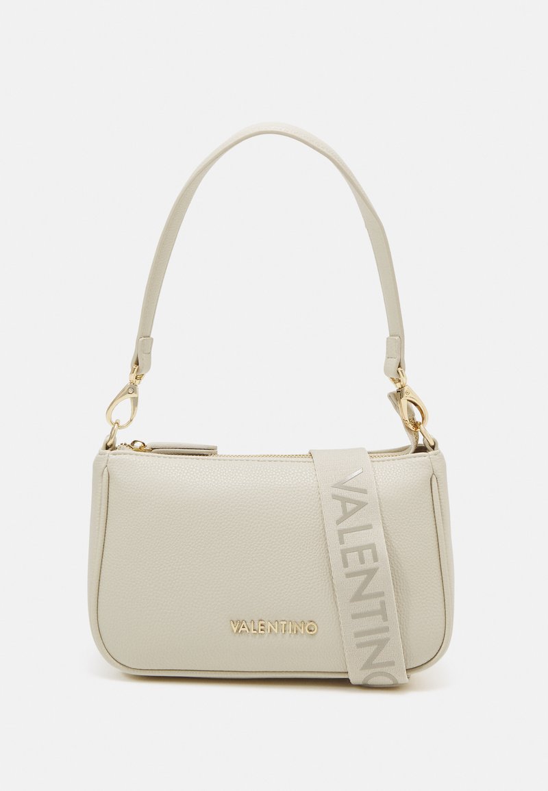 Beżowa skórzana torebka o zorganizowanej konstrukcji, z zamkiem błyskawicznym w kolorze złotym, paskiem z logo oraz teksturowaną powierzchnią. Udekorowana złotymi elementami.