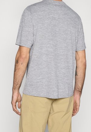 Šedé tričko s krátkým rukávem a kulatým výstřihem, vyrobené z texturované látky, s volným střihem a rovný lem, nošené s béžovými kalhotami.