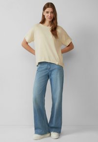 Beige kortom t-shirt met een relaxte pasvorm, gecombineerd met lichtblauwe wijde jeans en witte sneakers. Eenvoudig ontwerp met opgerolde mouwen.
