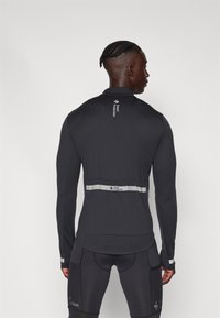 Svart langermet treningstopp med reflekterende stripe, glatt tekstur, tettsittende design og logodetalj på øvre rygg.