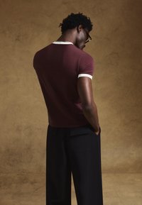 Burgundska vrh kratkih rokavov z belimi poudarki, v kombinaciji s črnimi hlačami. Majica ima oprijeto obliko in teksturirano tkanino.