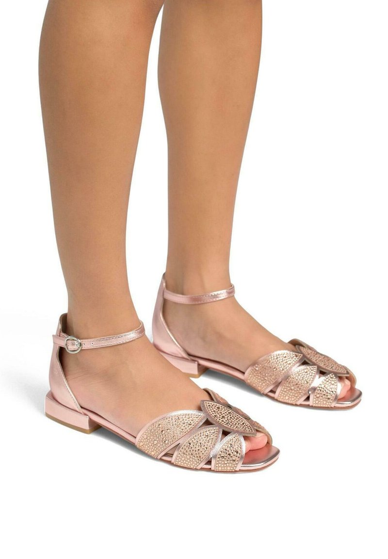 Des sandales rose clair avec un petit talon carré présentent une large bride frontale ornée d'un design décoratif et une bride de cheville avec une boucle.